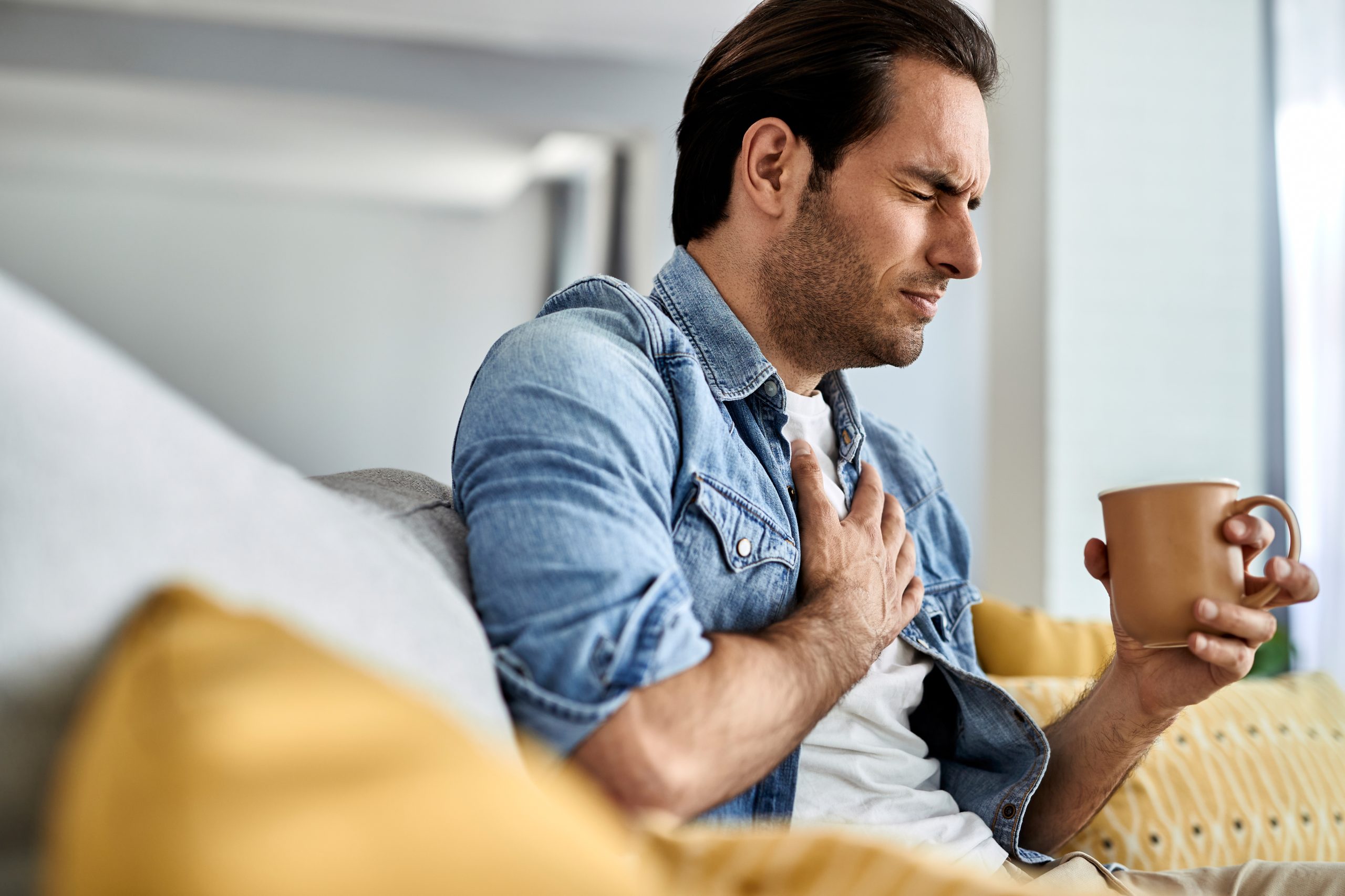 Young man having a chest pain while drinking tea at home.